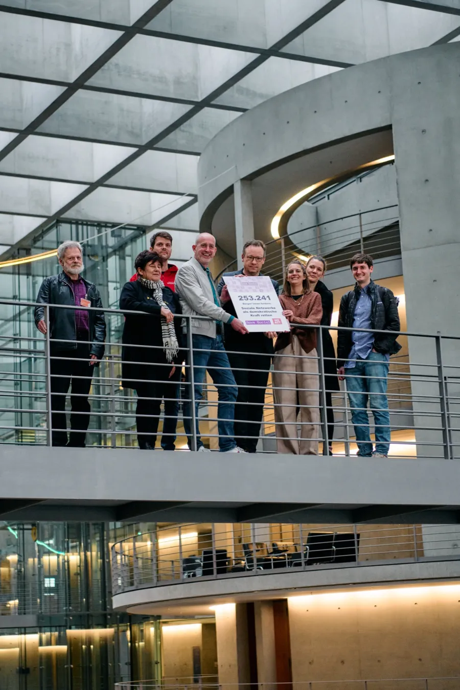 Gruppe auf einer Galerie mit einem Schild bei der &Uuml;bergabe der Petition in Berlin.